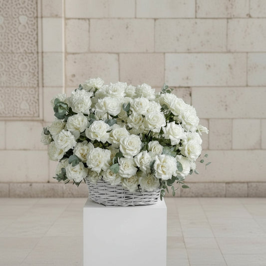 Bouquet of white flowers in a wicker basket on a white pedestal against a light tiled wall.