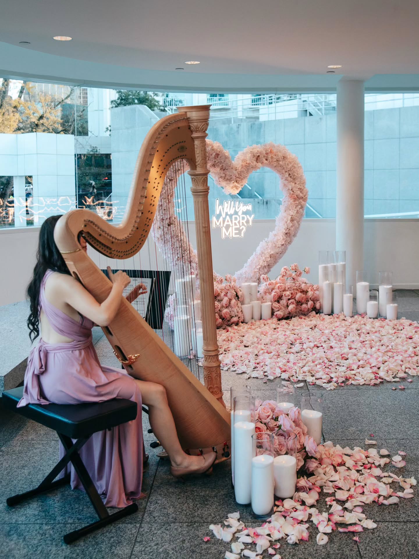 Woman playing a harp in a decorated room with pink flowers and candles.