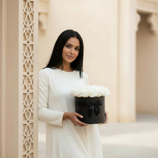 Woman holding a black box with white flowers against a neutral background