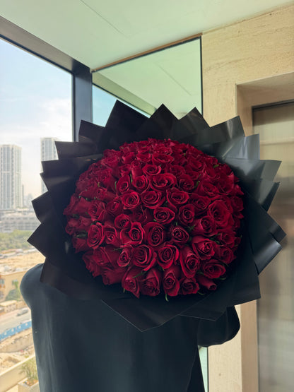 Bouquet of red roses wrapped in black paper on a table with a cityscape view.