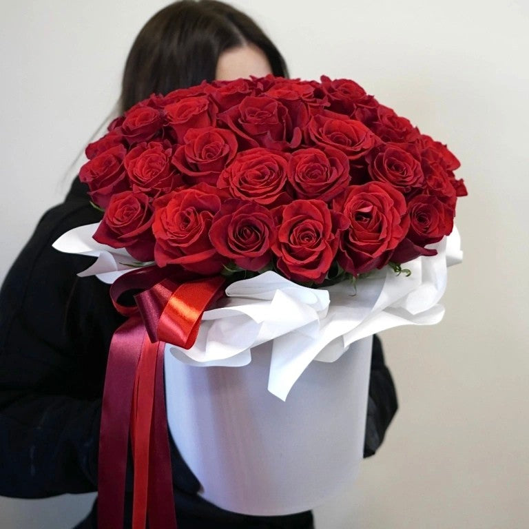 Person holding a large box of red roses with a white ribbon.