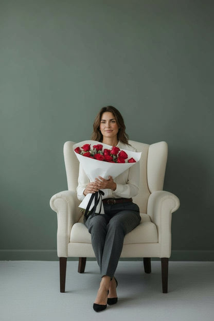 Woman sitting in a chair holding a bouquet of red flowers against a plain background