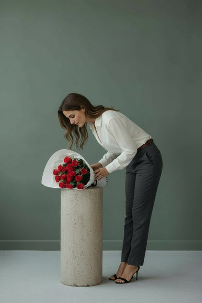 Woman arranging flowers on a cylindrical concrete stand against a plain background
