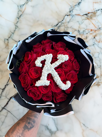 Bouquet of red roses with a white letter 'K' on a marble surface