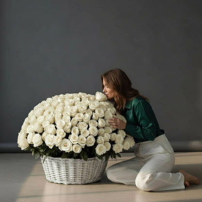 Woman kneeling next to a large basket of white roses against a dark background