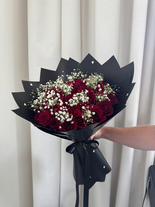 Bouquet of red roses and white flowers wrapped in black paper held against a white curtain background