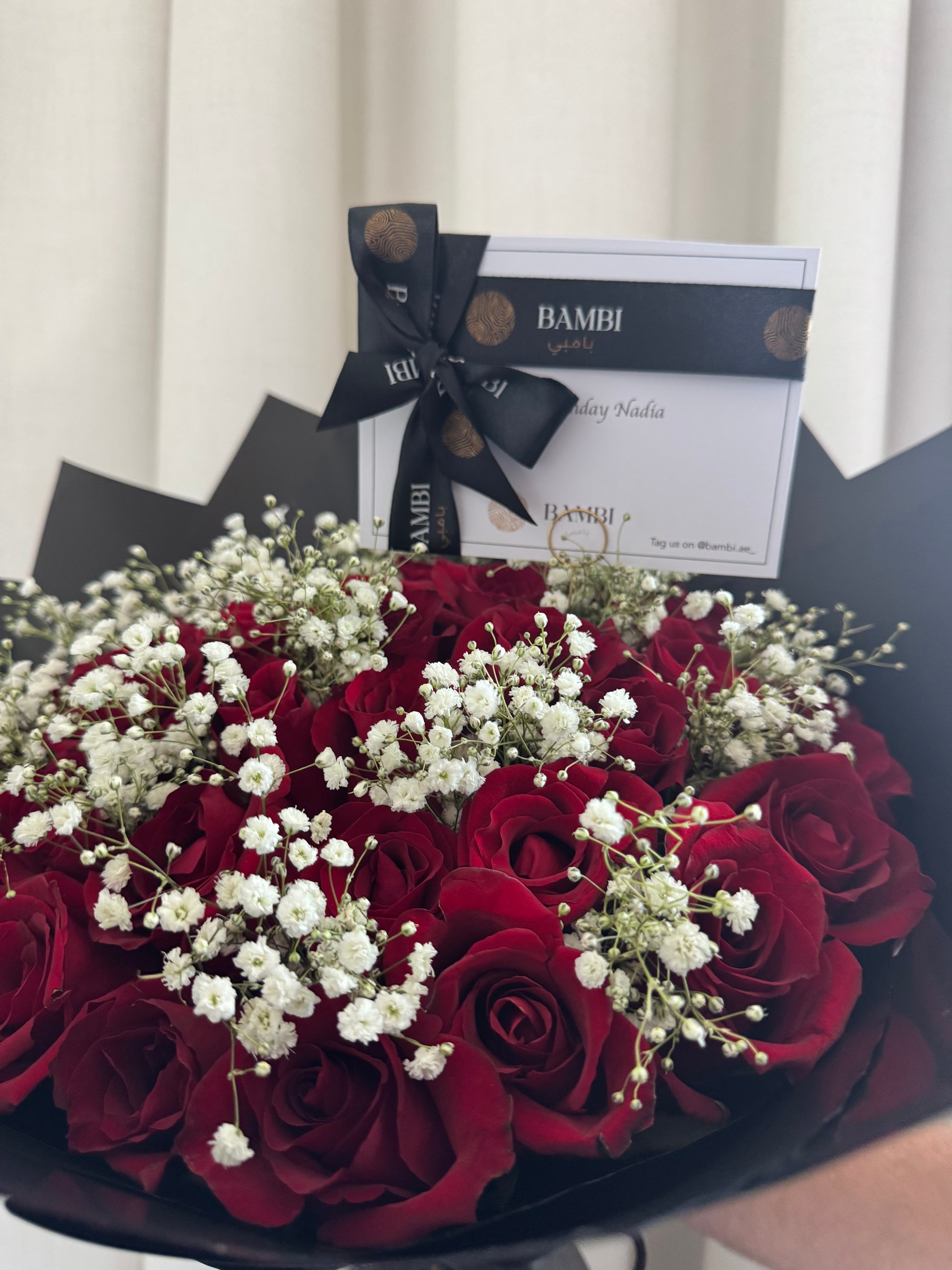 Bouquet of red roses with white flowers and a Bambi gift box in the background.