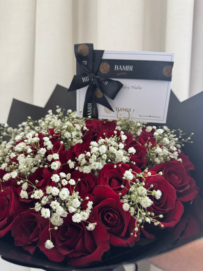 Bouquet of red roses with white flowers and a Bambi gift box in the background.