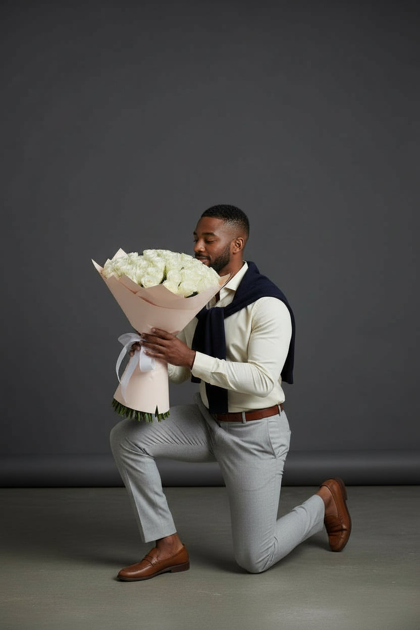 Man kneeling and holding a bouquet of white flowers against a gray background