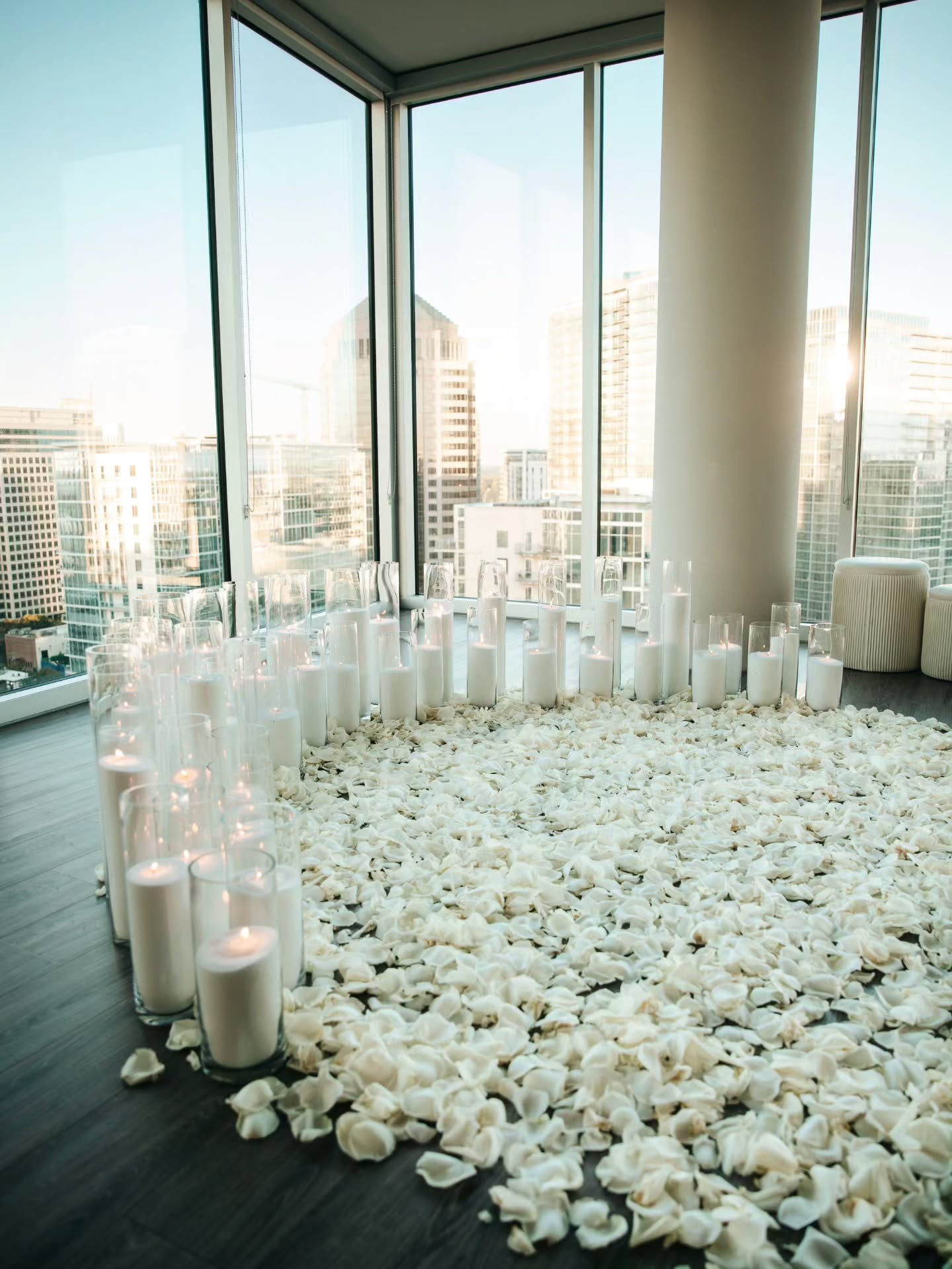 Decorative setup with candles and white petals in a room with large windows.