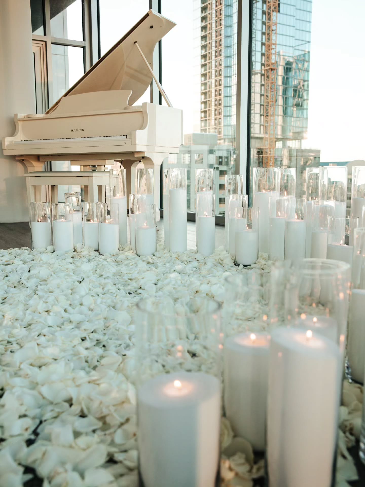 White grand piano with candles and pebbles in a room with large windows.