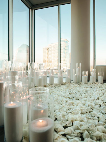 White candles on a pebble surface with large windows in the background