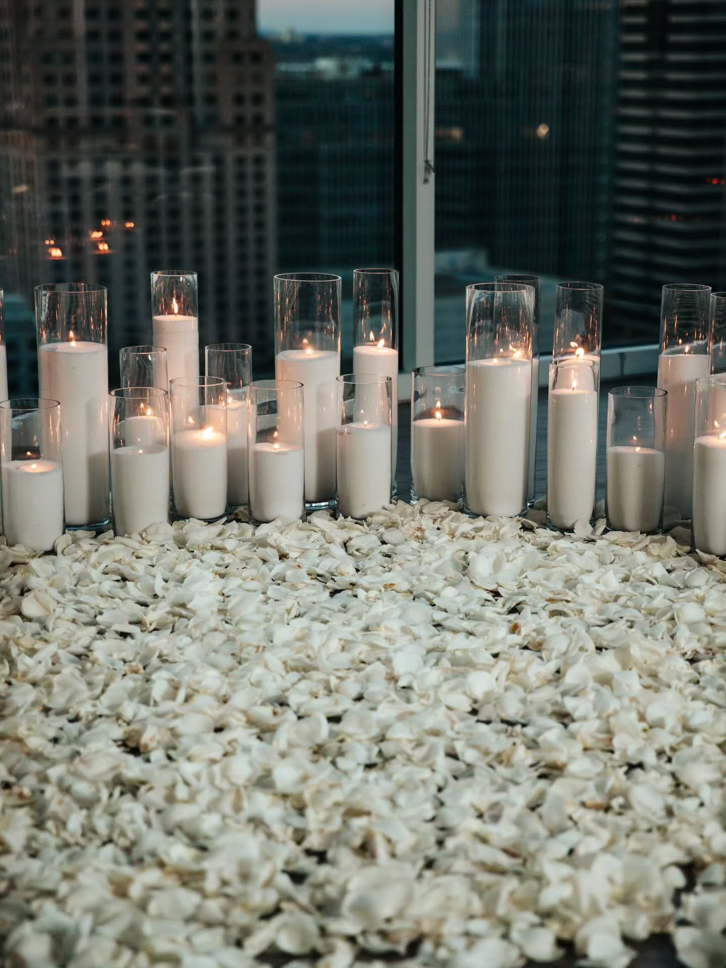 Candles in glass holders on a bed of white pebbles with a cityscape background