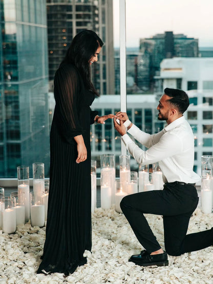 Man proposing to a woman on a rooftop with candles and cityscape background