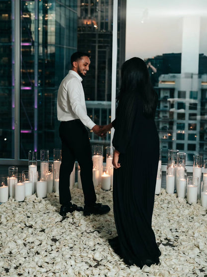 Man and woman holding hands on a rooftop with candles and cityscape background
