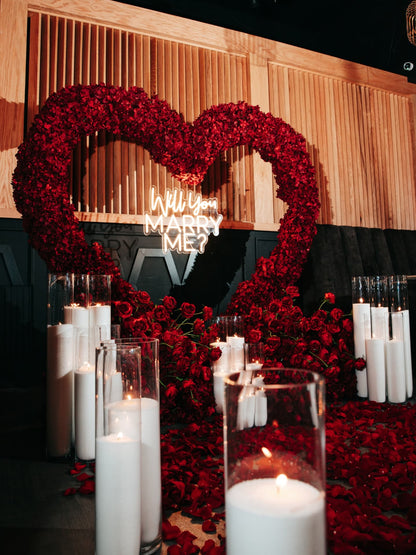 Heart-shaped arrangement of red roses with candles on a dark background