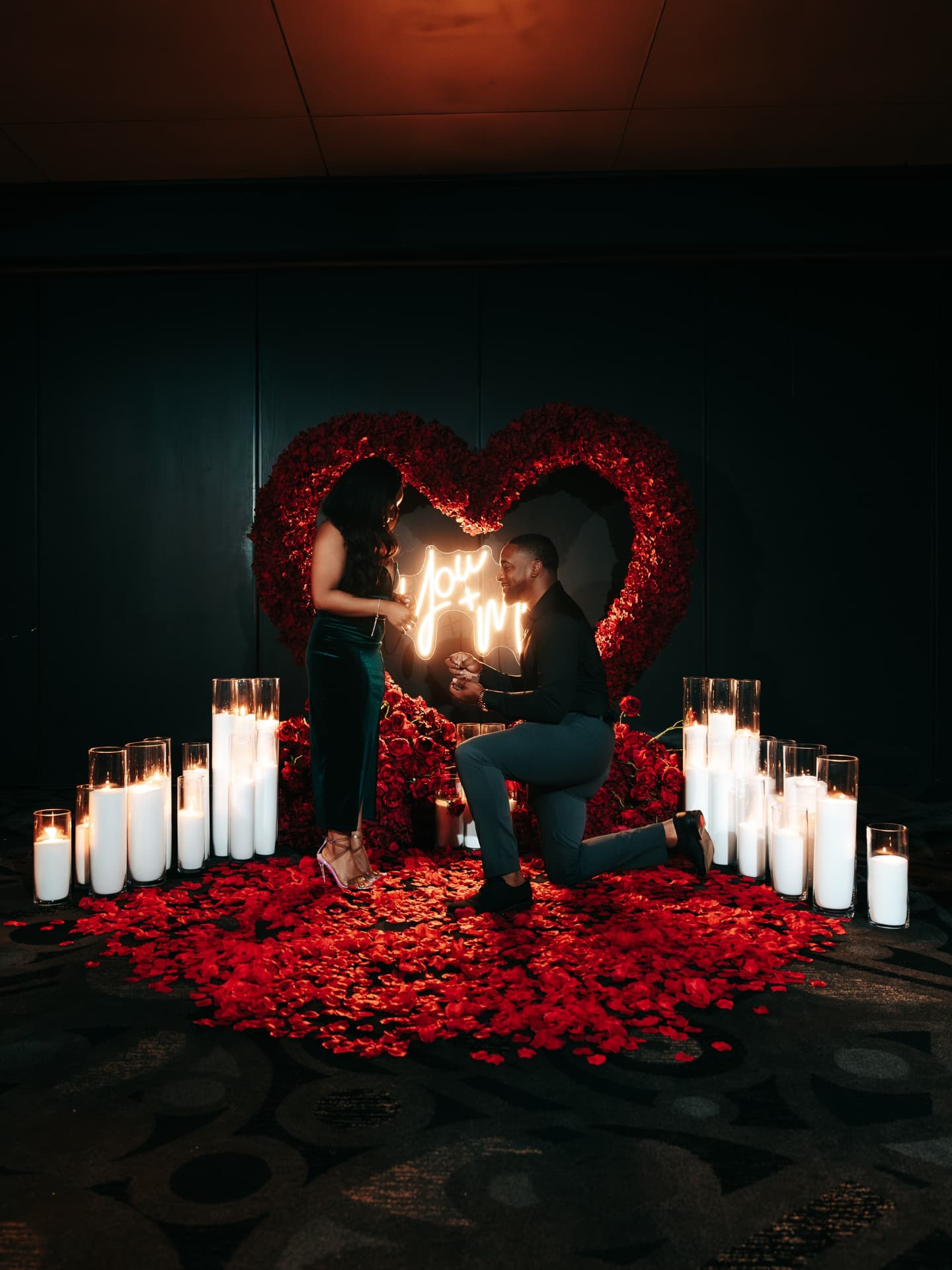 Couple in a romantic setting with candles and heart-shaped decorations.