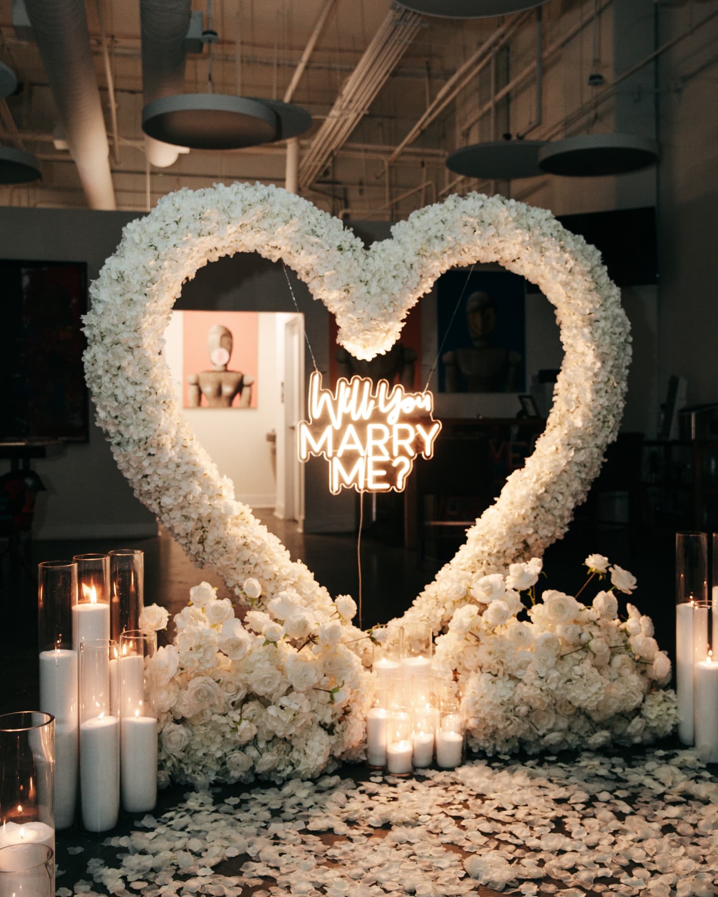 Heart-shaped floral arrangement with 'Will you marry me?' neon sign in a dimly lit room.