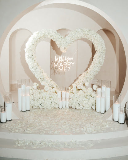 Heart-shaped floral arrangement with 'Will you marry me?' message in a romantic setting.