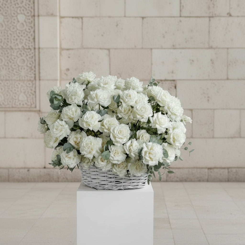Bouquet of white flowers in a wicker basket on a white pedestal against a light tiled wall.