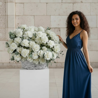 Woman in a blue dress holding a large arrangement of white flowers against a light stone wall.