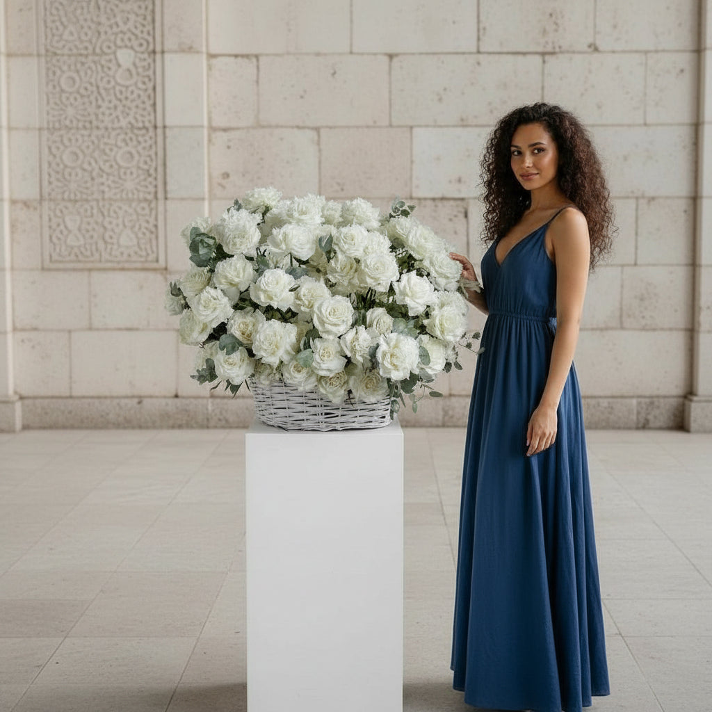 Woman in a blue dress standing next to a large bouquet of white flowers on a pedestal.