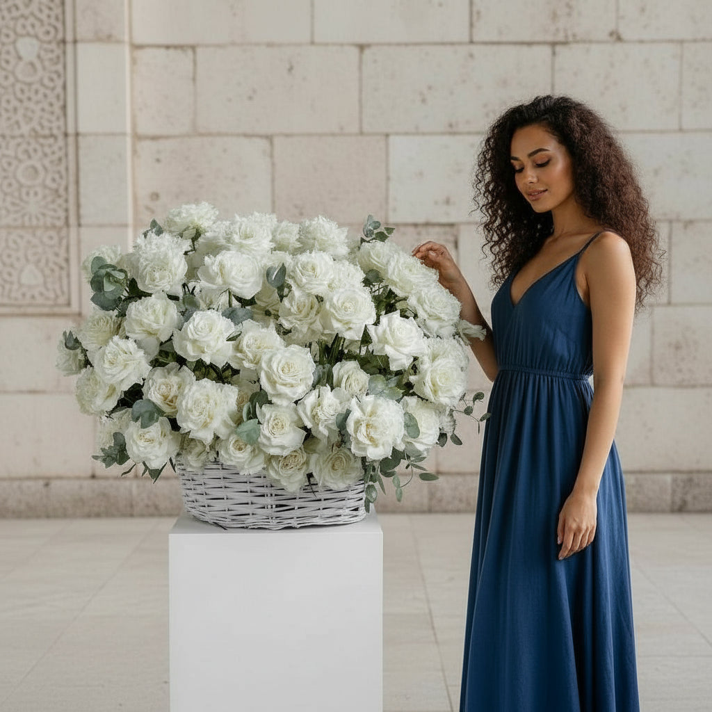 Woman in a blue dress standing next to a large arrangement of white flowers in a wicker basket.