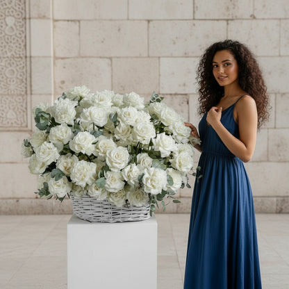 Woman in a blue dress holding a large arrangement of white flowers against a stone wall.