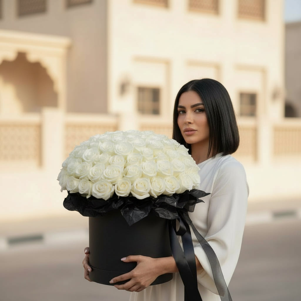 Woman holding a large bouquet of white roses in a black box with a blurred building in the background