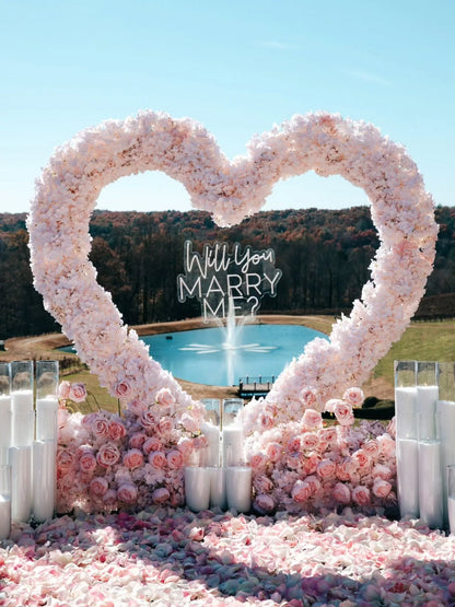 Heart-shaped floral arrangement with 'Will You Marry Me?' question at a scenic location.