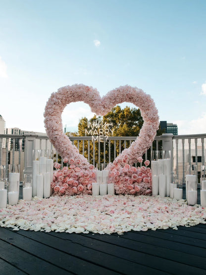Heart-shaped floral arrangement with 'Will You Marry Me?' proposal sign on a rooftop.
