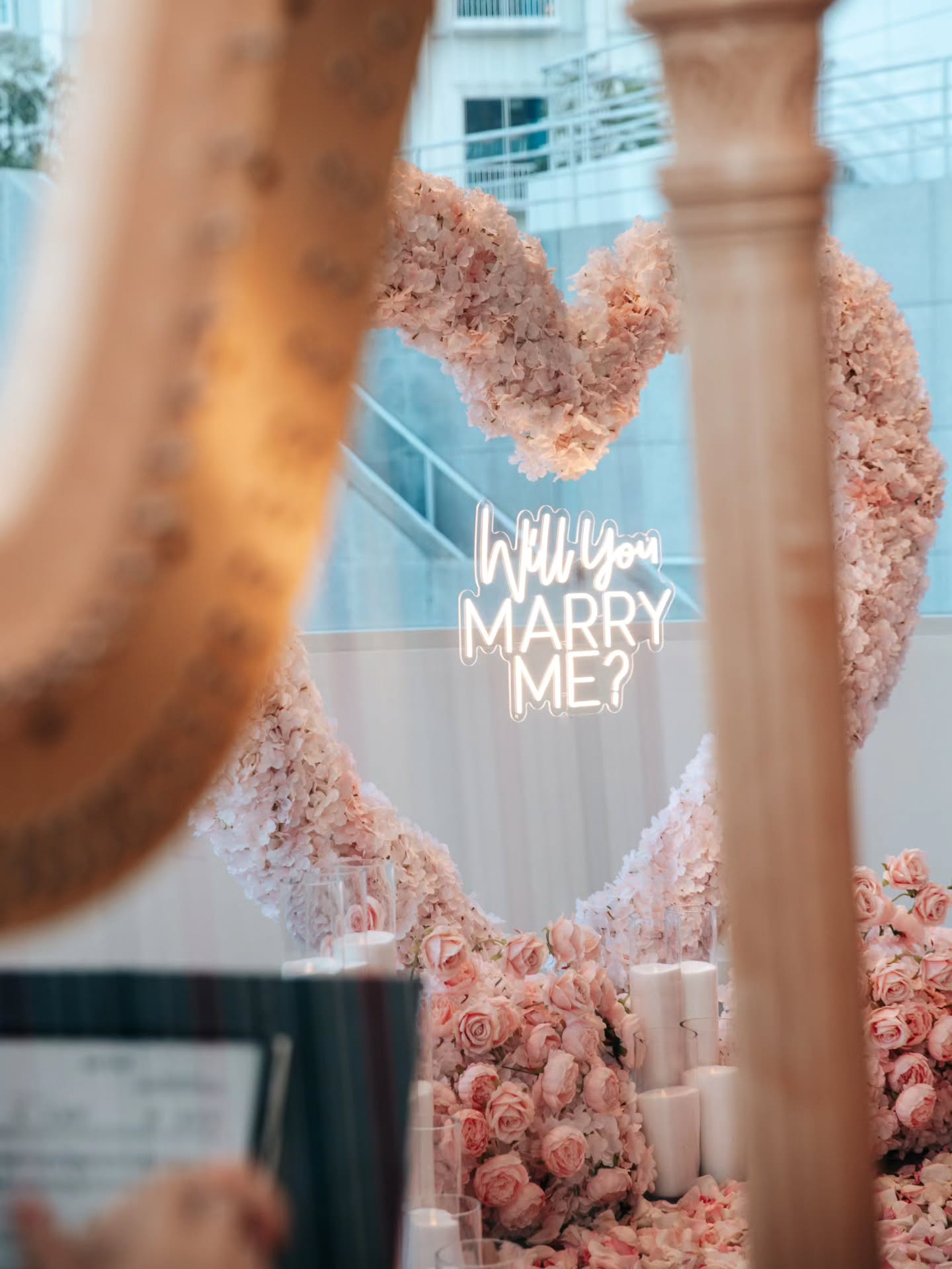 Floral arrangement shaped like a heart with 'Will You Marry Me?' text, blurred background