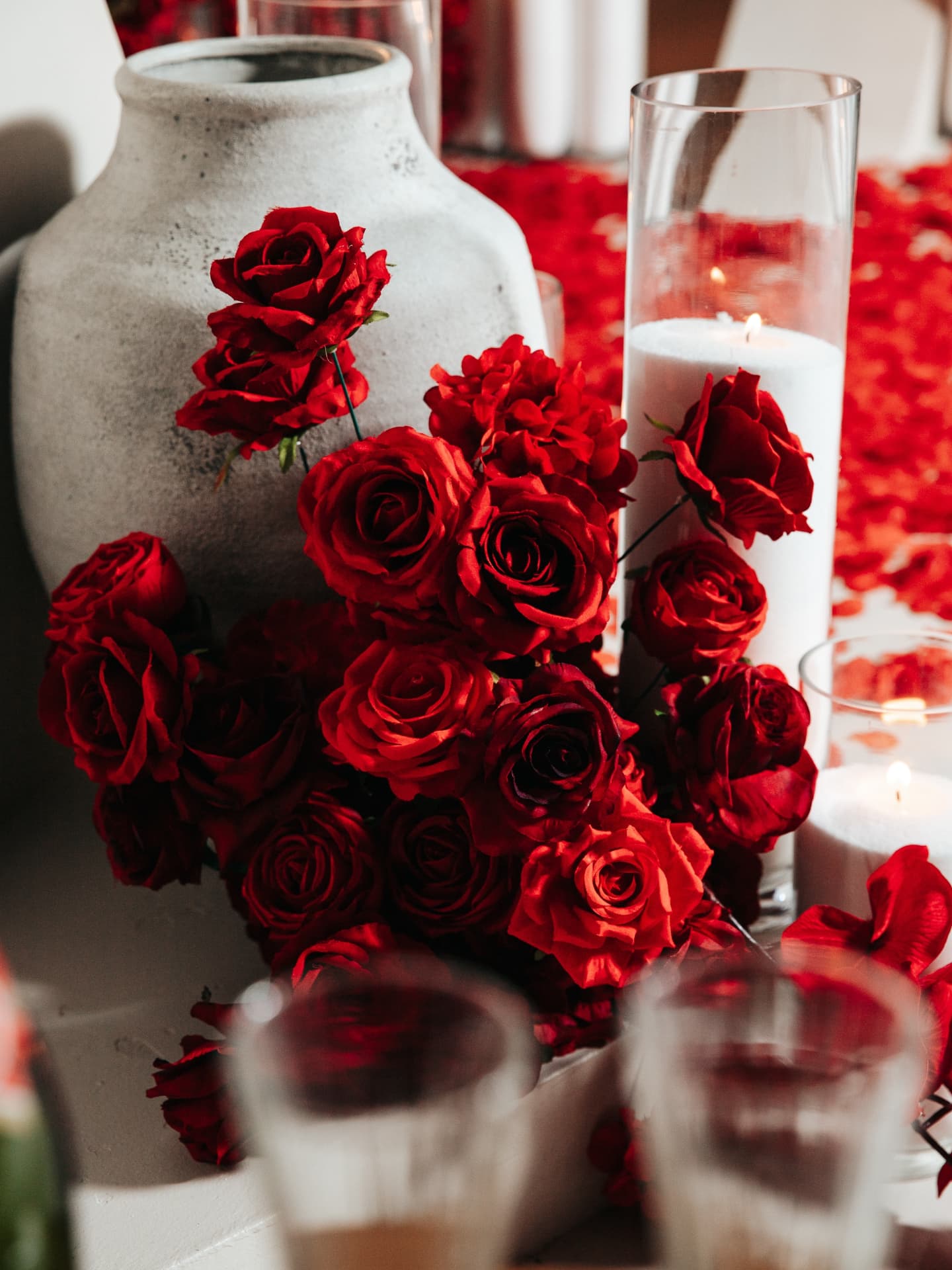 Bouquet of red roses in a white vase on a table with candles and glasses.