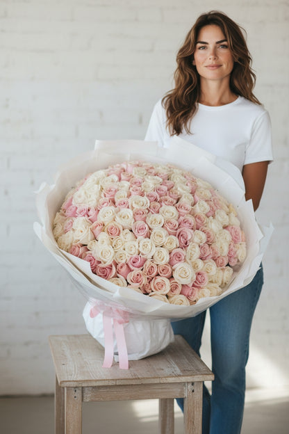 Woman holding a large bouquet of pink and white roses in a white room.
