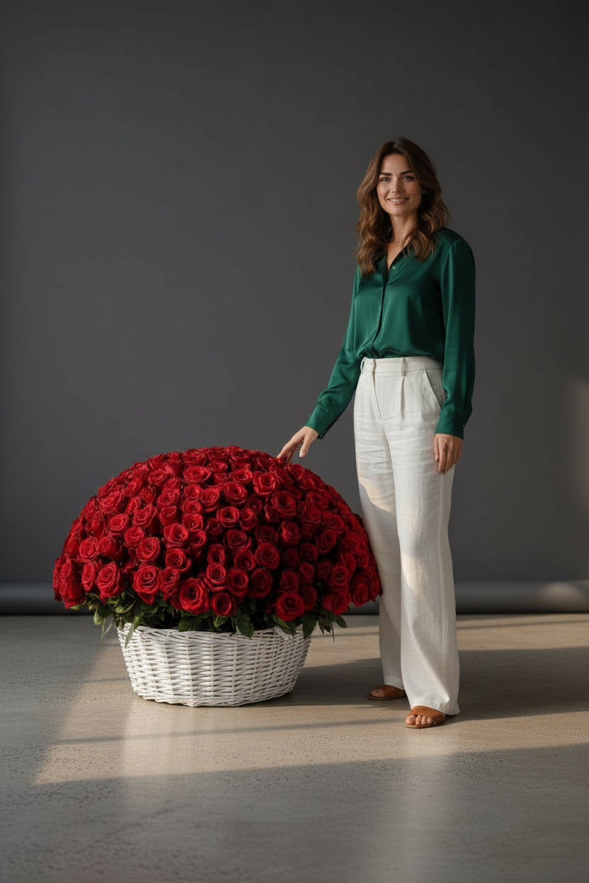 Woman standing next to a large arrangement of red roses in a white basket on a gray floor.