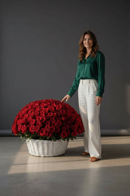 Woman standing next to a large arrangement of red roses in a white basket on a gray floor.