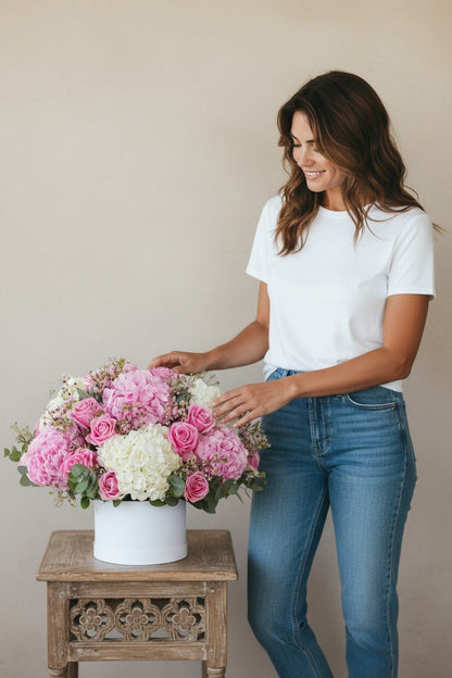 Woman holding a bouquet of pink and white flowers next to a wooden table with a floral arrangement.