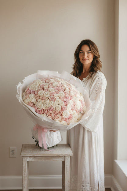 Woman holding a large bouquet of pink and white roses in a softly lit room.