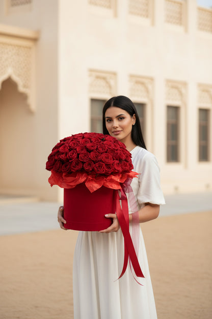 Woman holding a large bouquet of red roses in an outdoor setting with architectural elements.