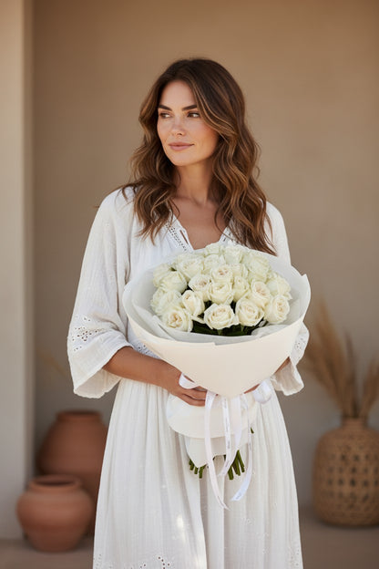Woman holding a bouquet of white roses in a softly lit room with neutral decor.